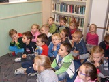Zasłuchane przedszkolaki siedzą na dywanie w bibliotece
