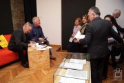 F. Tomaszkiewicz podpisuje książki, na pierwszym planie gablota z dokumentami 